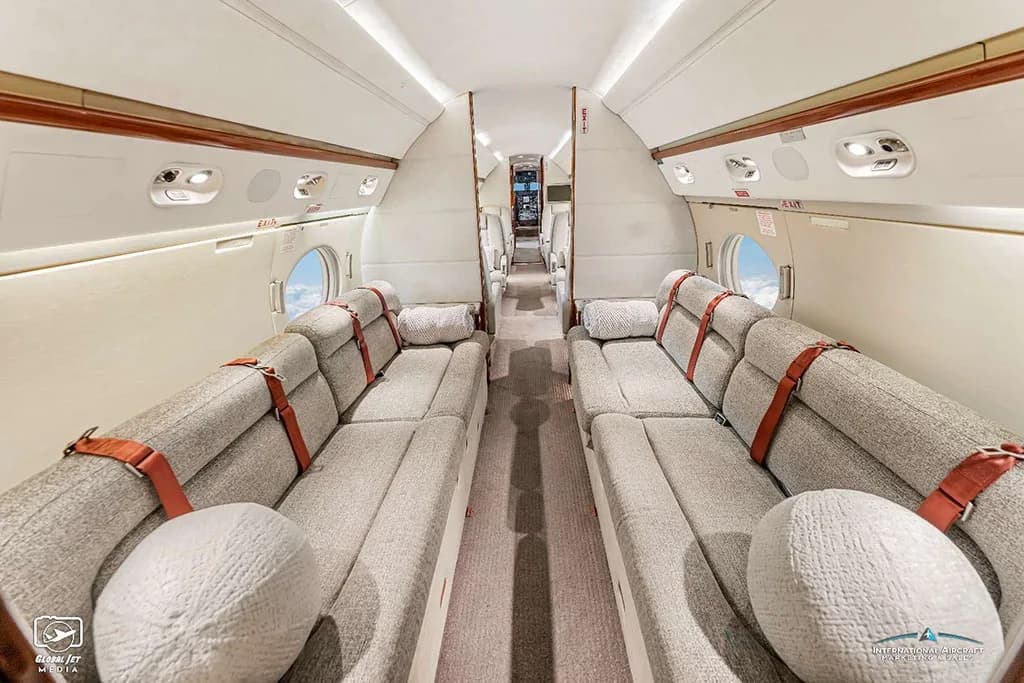 The aft cabin lounge area of a Gulfstream G550, featuring two long grey fabric sofas facing each other.