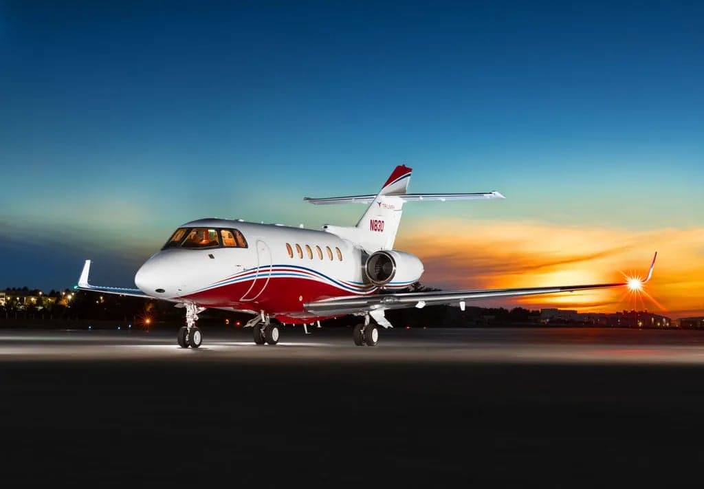 A Falcon aircraft with red and white paint scheme is parked on the tarmac at dusk.