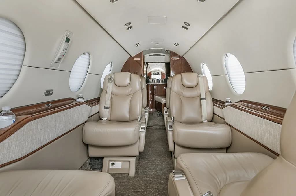 The luxurious interior cabin of a business jet, featuring beige leather seats and wood accents, looking towards the rear.