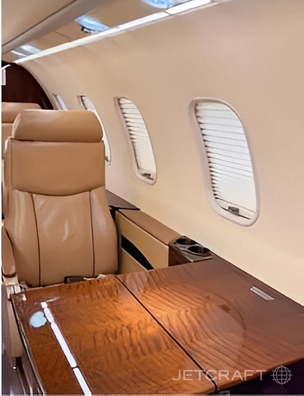 Tan leather seats and a wooden fold-out table next to windows with blinds in the aircraft cabin.