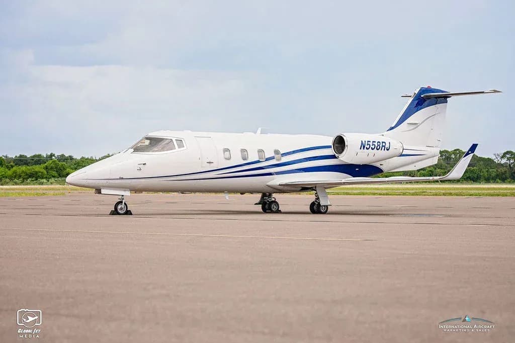 A white business jet with blue stripes, tail number N558RJ, parked on an airfield under a partly cloudy sky.