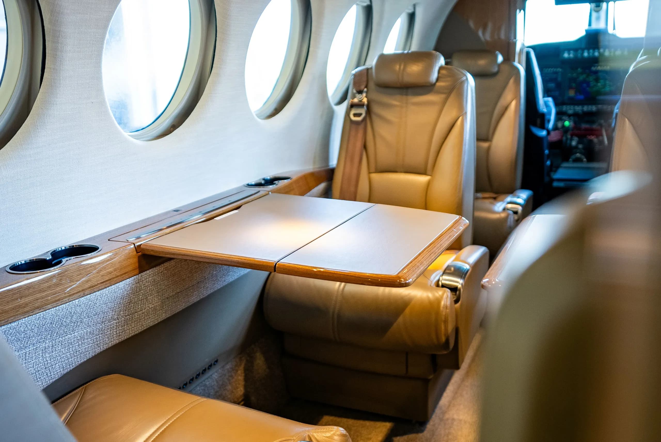 A close-up of a tan leather aircraft seat with a fold-out table extended, looking towards the cockpit.