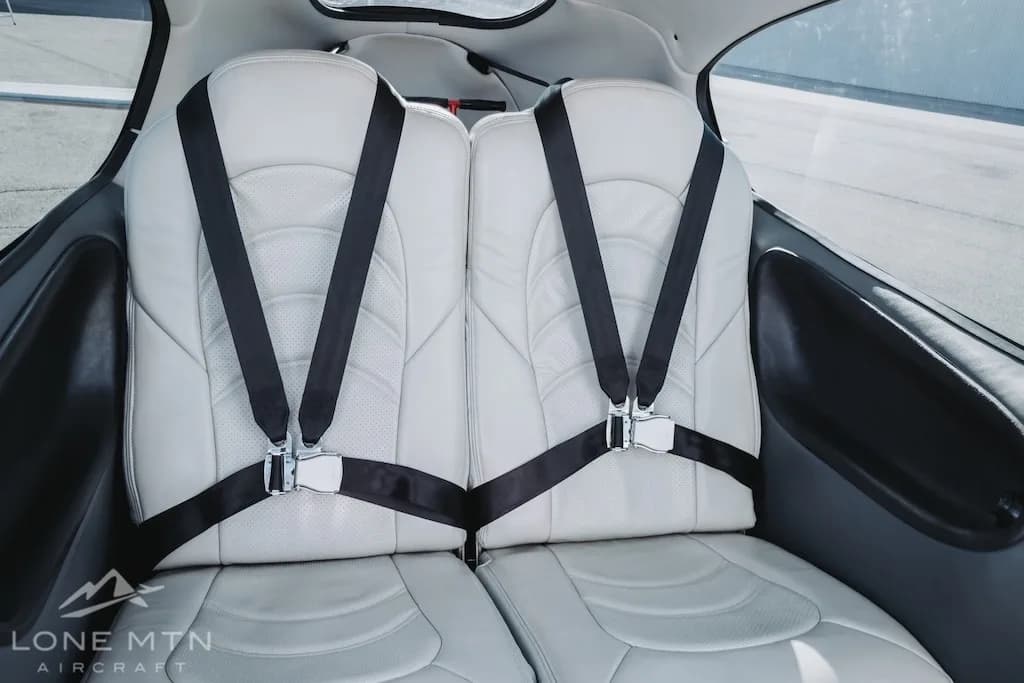 A close-up view of the light-colored leather rear seats with black harnesses in the Cirrus SR22 aircraft.