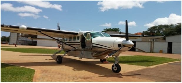A white twin-engine propeller aircraft with black stripes and an open passenger door is parked on an asphalt apron.