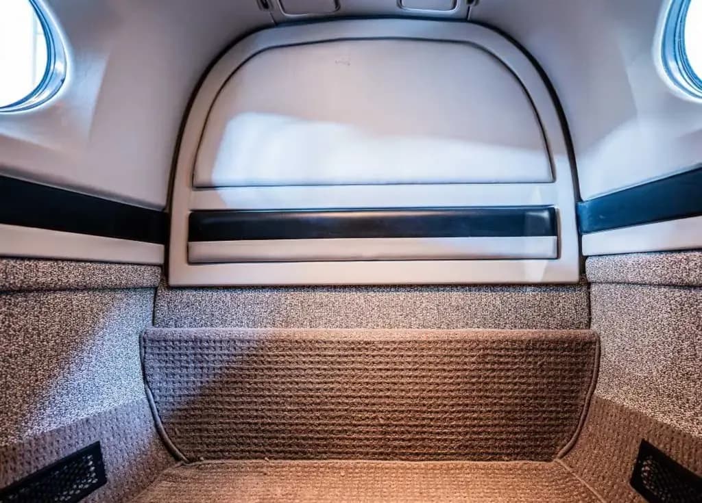 The rear interior section of an aircraft cabin, showing a carpeted floor and a storage area.