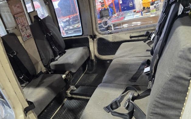 The interior cabin of a helicopter features grey passenger seats with seatbelts.