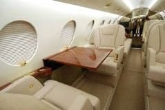 The aircraft's interior features a wooden table and cream-colored leather seats.