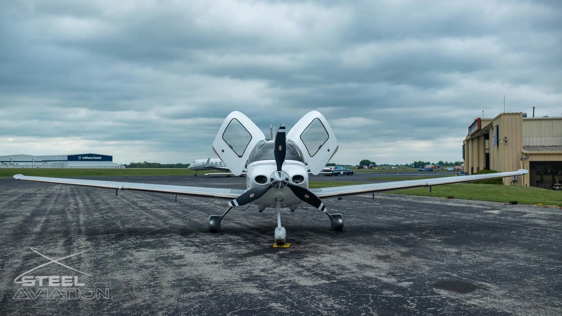 A white and silver Cirrus SR22T aircraft with its gull-wing doors open is seen from the front on an airfield.