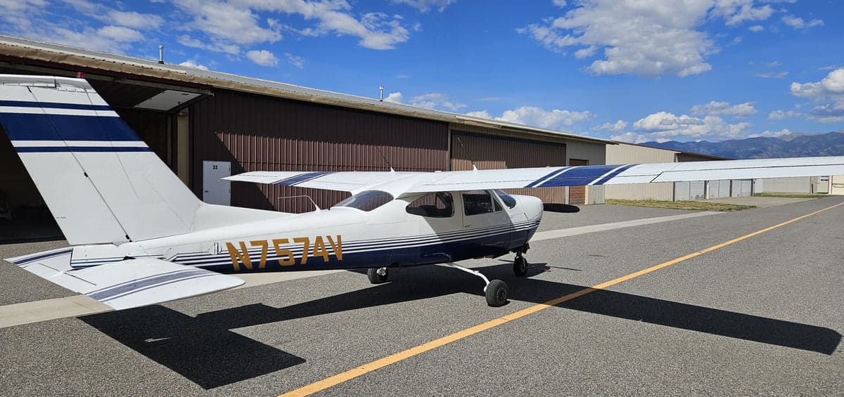 A Cessna 182 Skylane, tail number N7574V, parked on the tarmac in front of a hangar.