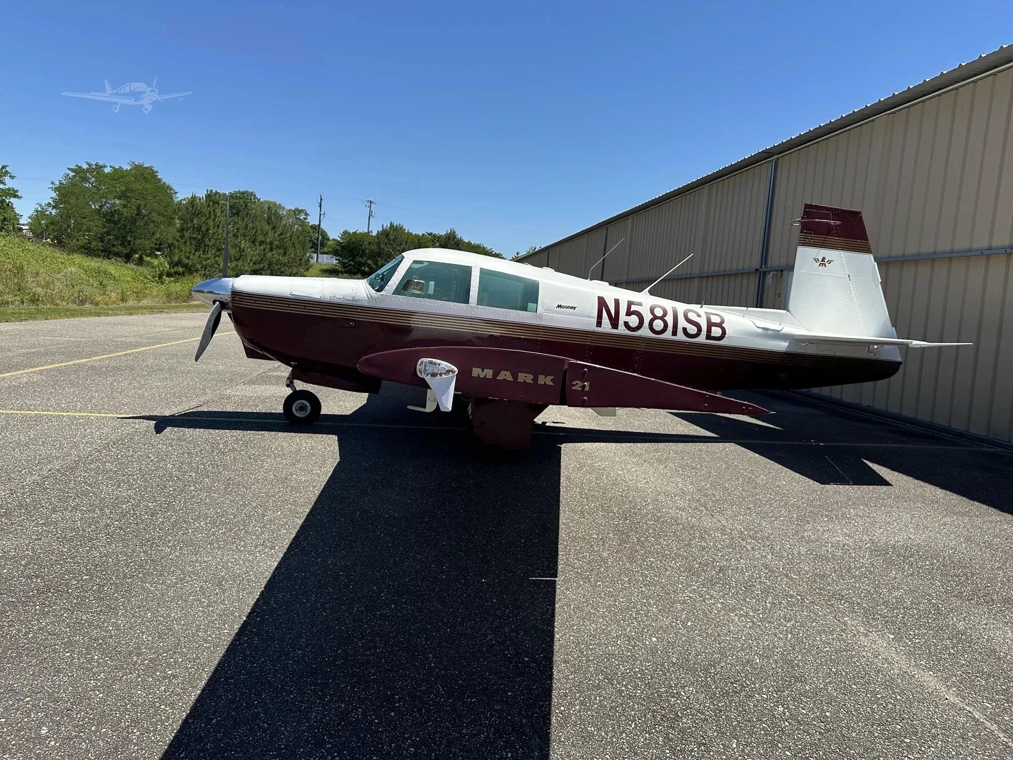 A side view of the white and maroon Mooney M20 Mark 21 aircraft, registration N581SB, parked on an asphalt ramp.