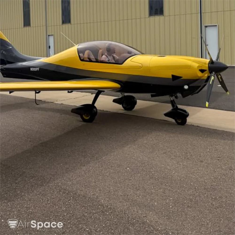 A yellow and black Freccia F200 aircraft with N900PF on the fuselage, parked on an asphalt ramp next to a hangar.