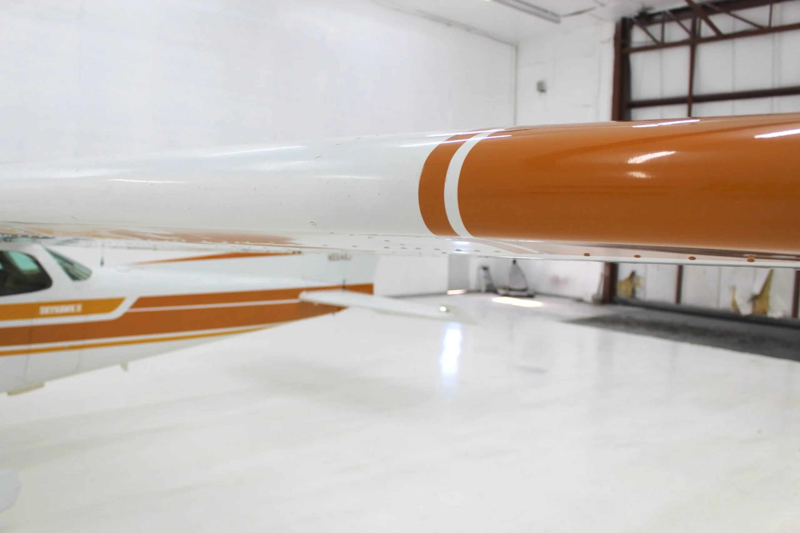 A close-up view of the white and orange wing of a Cessna Skyhawk II, with the fuselage in the background.