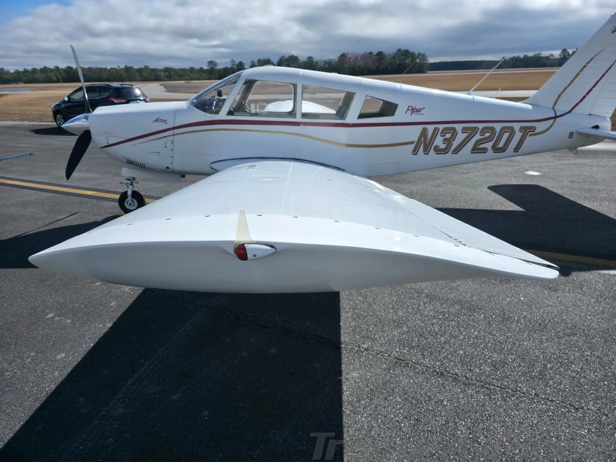 A close-up side view of the white Piper Arrow N3720T, showing the wing and fuselage with gold and red stripes.