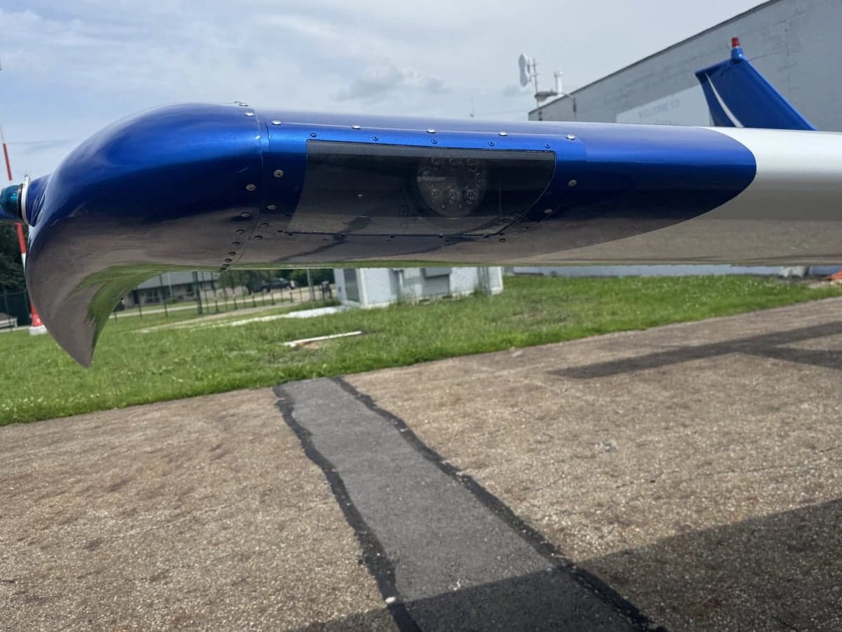 A close-up view of the blue wingtip of a white aircraft, showing a landing light and navigation light.