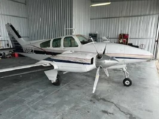 A white and blue twin-engine aircraft, N55EZ, is parked inside a hangar, viewed from the front-right.