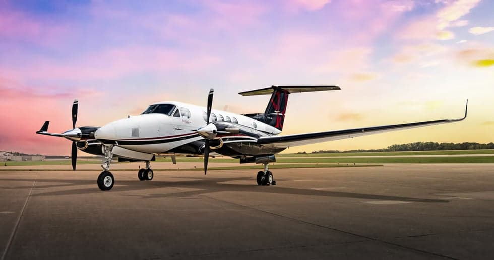 A Beechcraft King Air twin-turboprop aircraft on the ramp with a colorful sunset in the background.