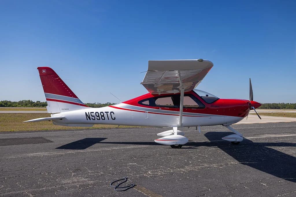 A side view of a red and white Tecnam P2010 aircraft with registration N598TC parked on an airfield.