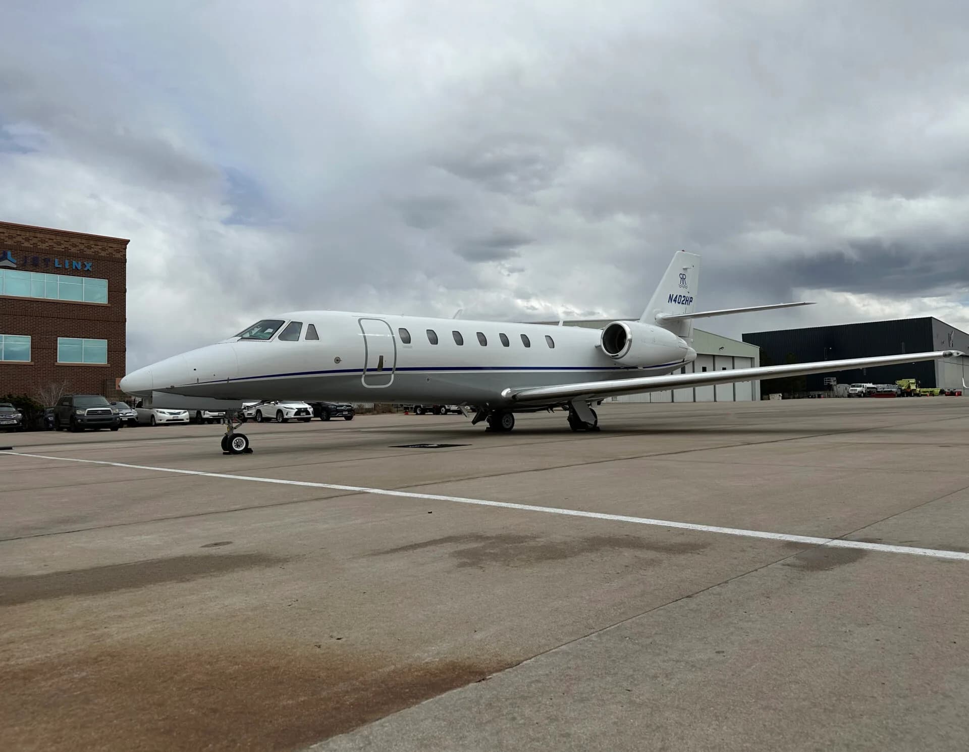 A white business jet with blue accents and registration N402BP parked on an airport tarmac under a cloudy sky.