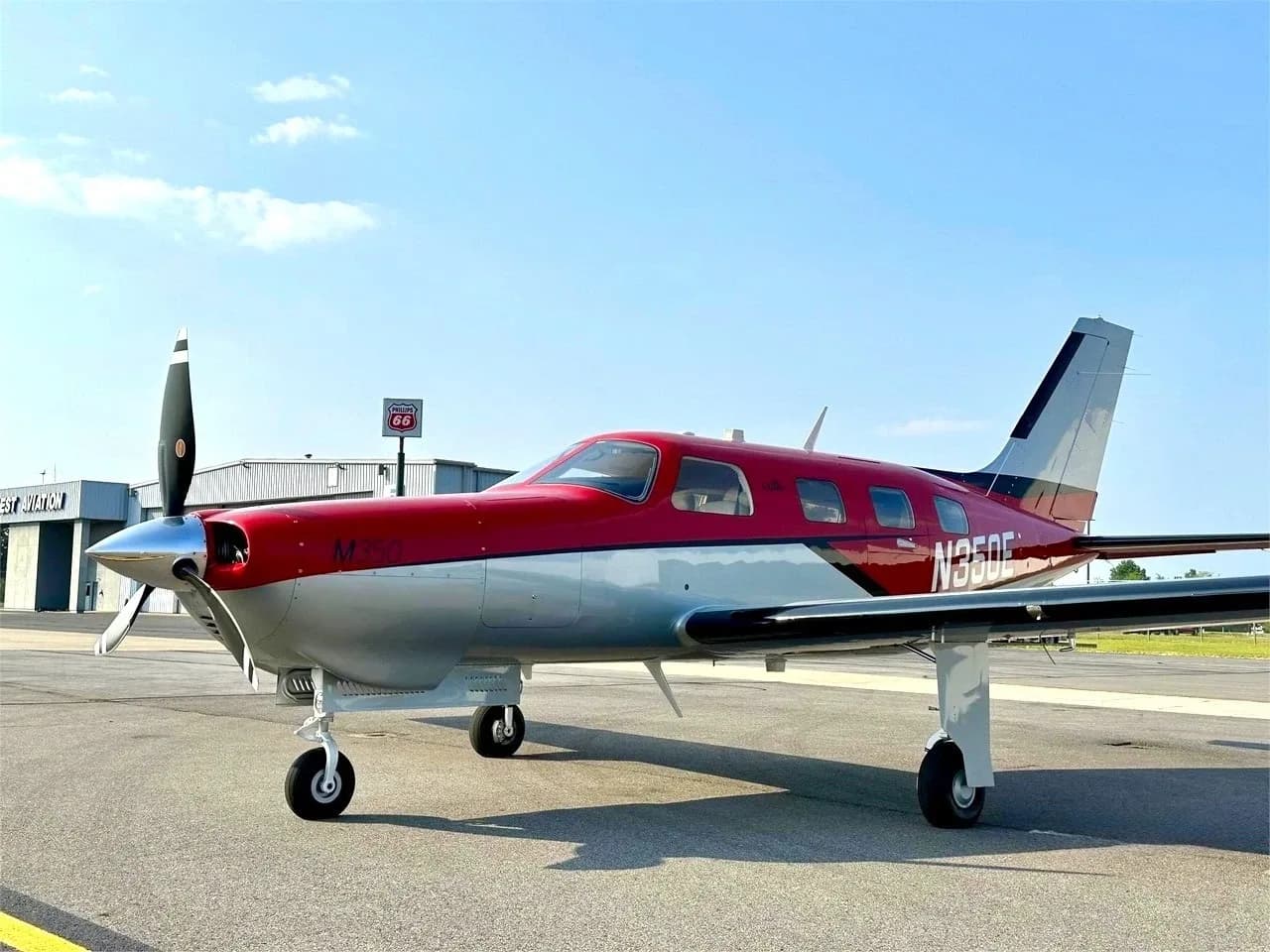A red and silver Piper M350 aircraft, registration N350E, parked on an airport tarmac under a blue sky.