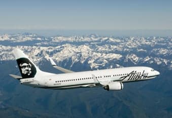 Alaska Airlines Boeing 737 flying over snow-capped mountains.