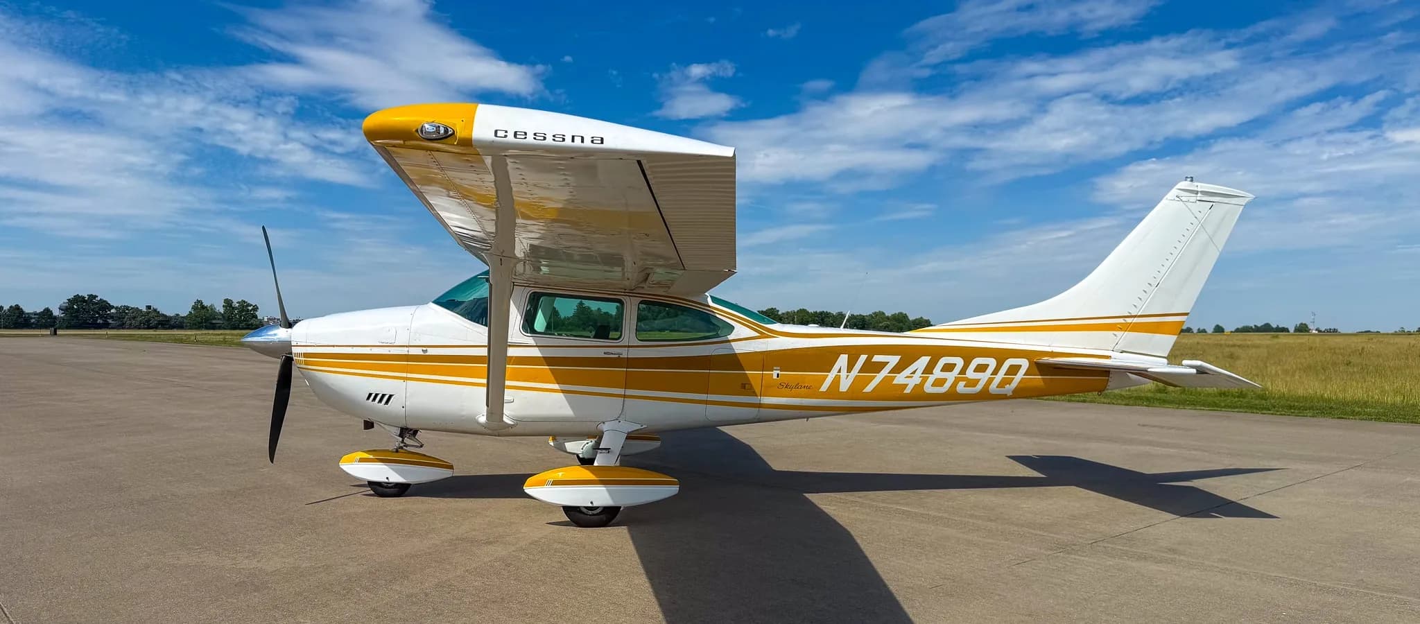 A white and gold Cessna Skylane N7489Q is parked on an airfield tarmac, viewed from the right side.