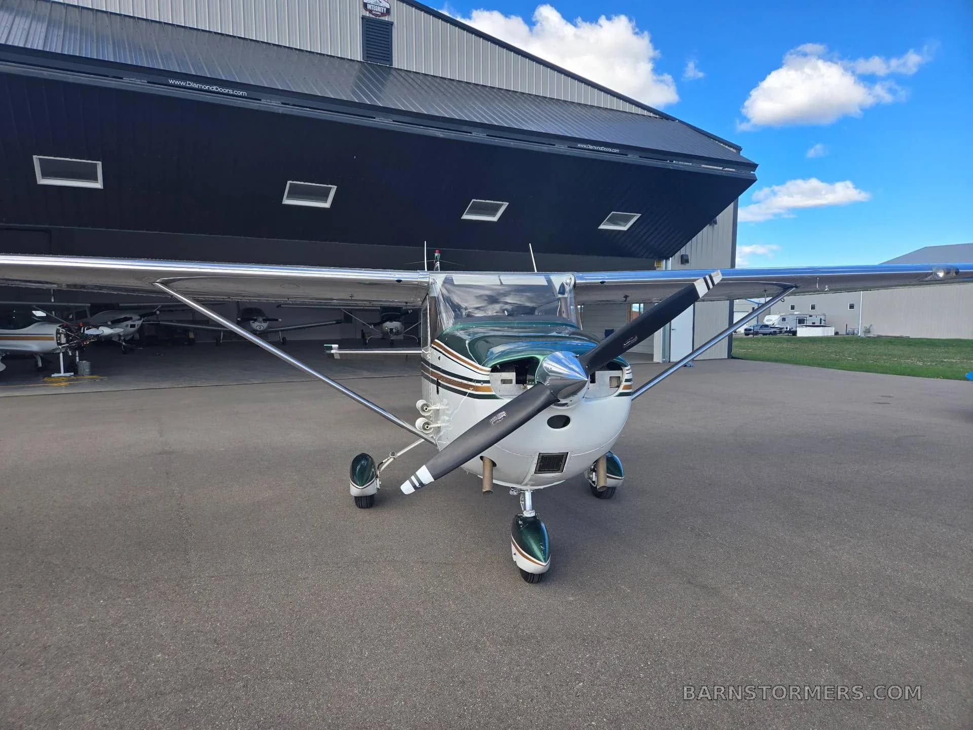 A white and green Cessna 172 is parked head-on on the tarmac in front of an open hangar.