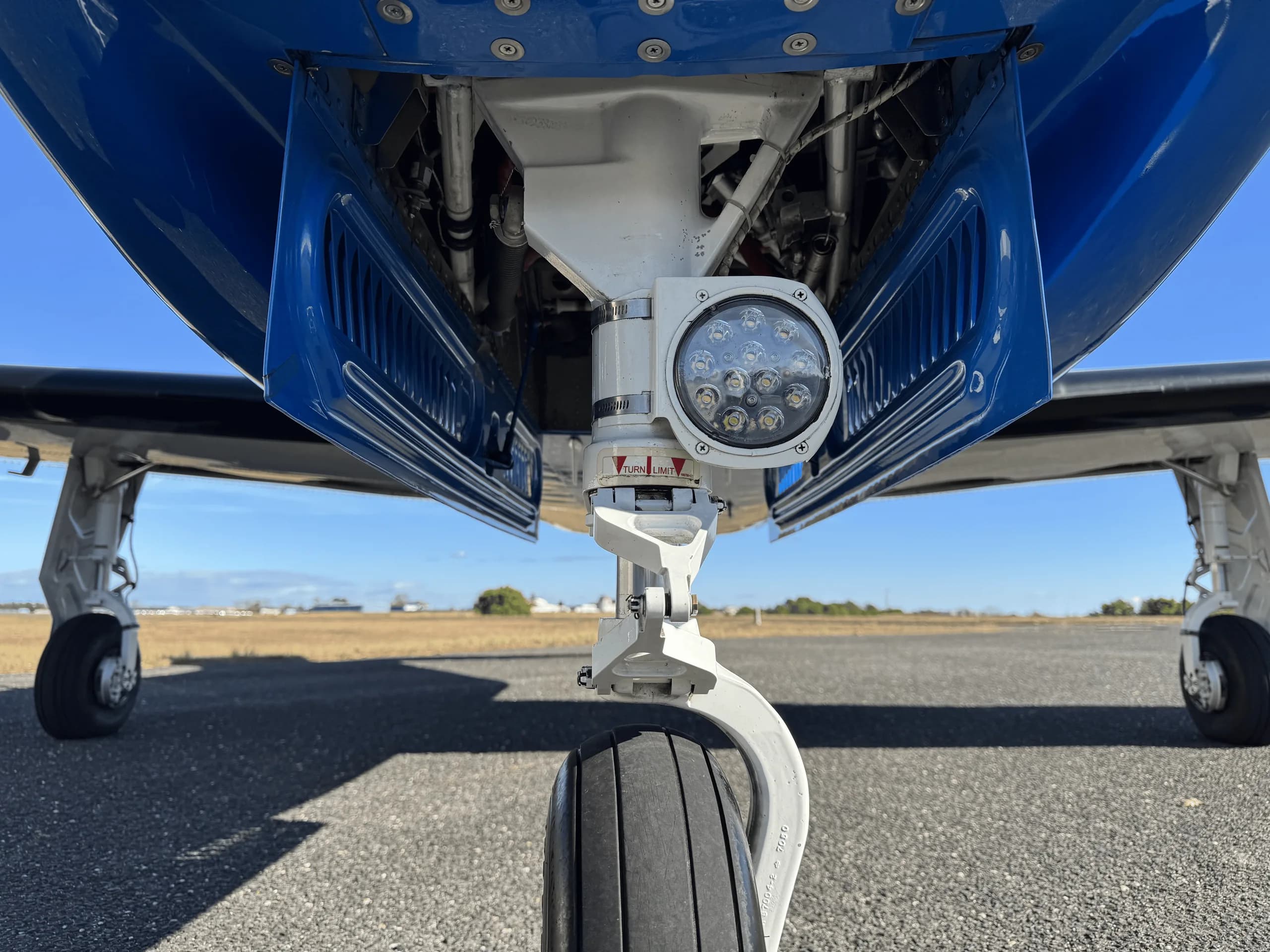 A close-up, low-angle view of the nose landing gear of a Piper M350 aircraft on an airfield.