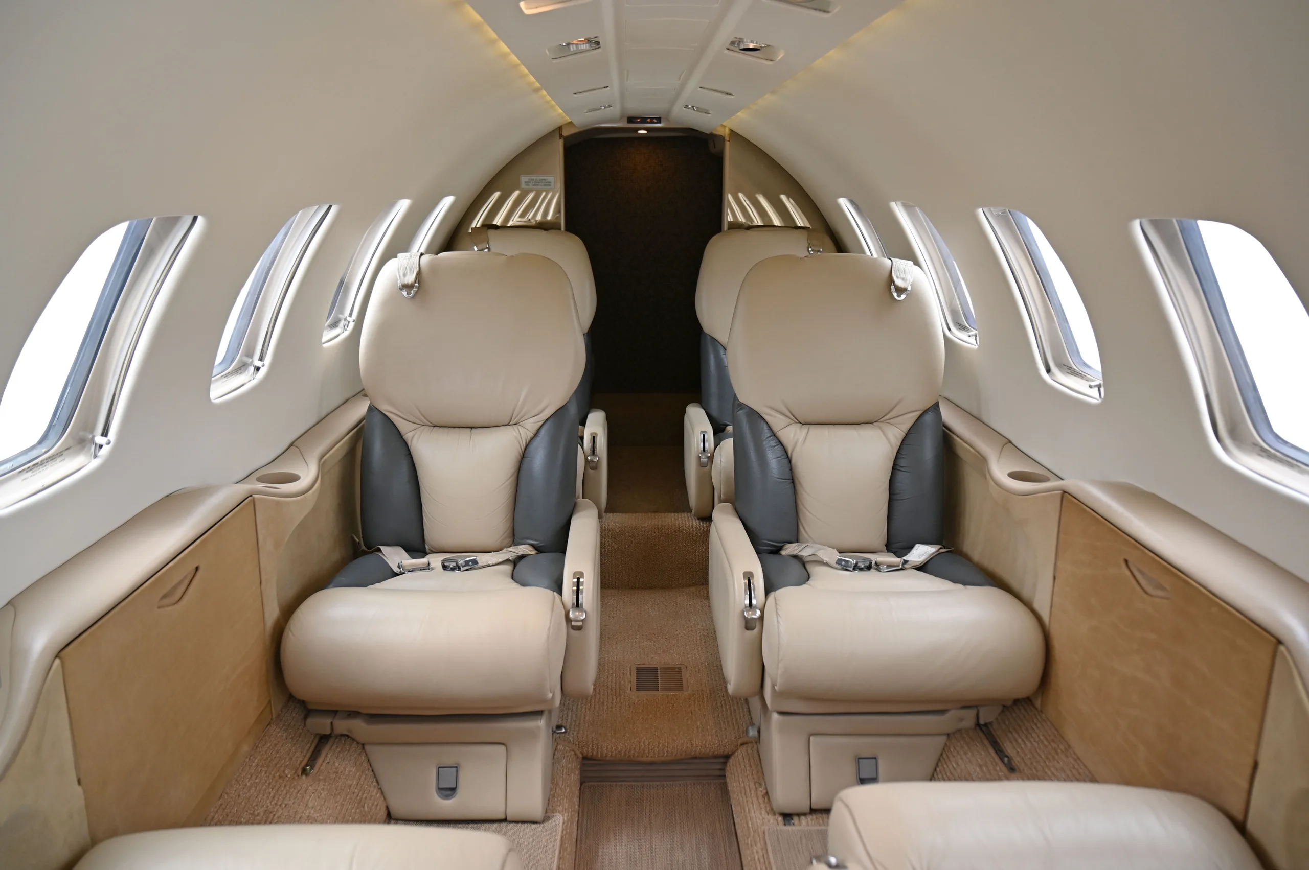 The interior cabin of a private jet, showing two rows of beige and gray leather seats facing each other.