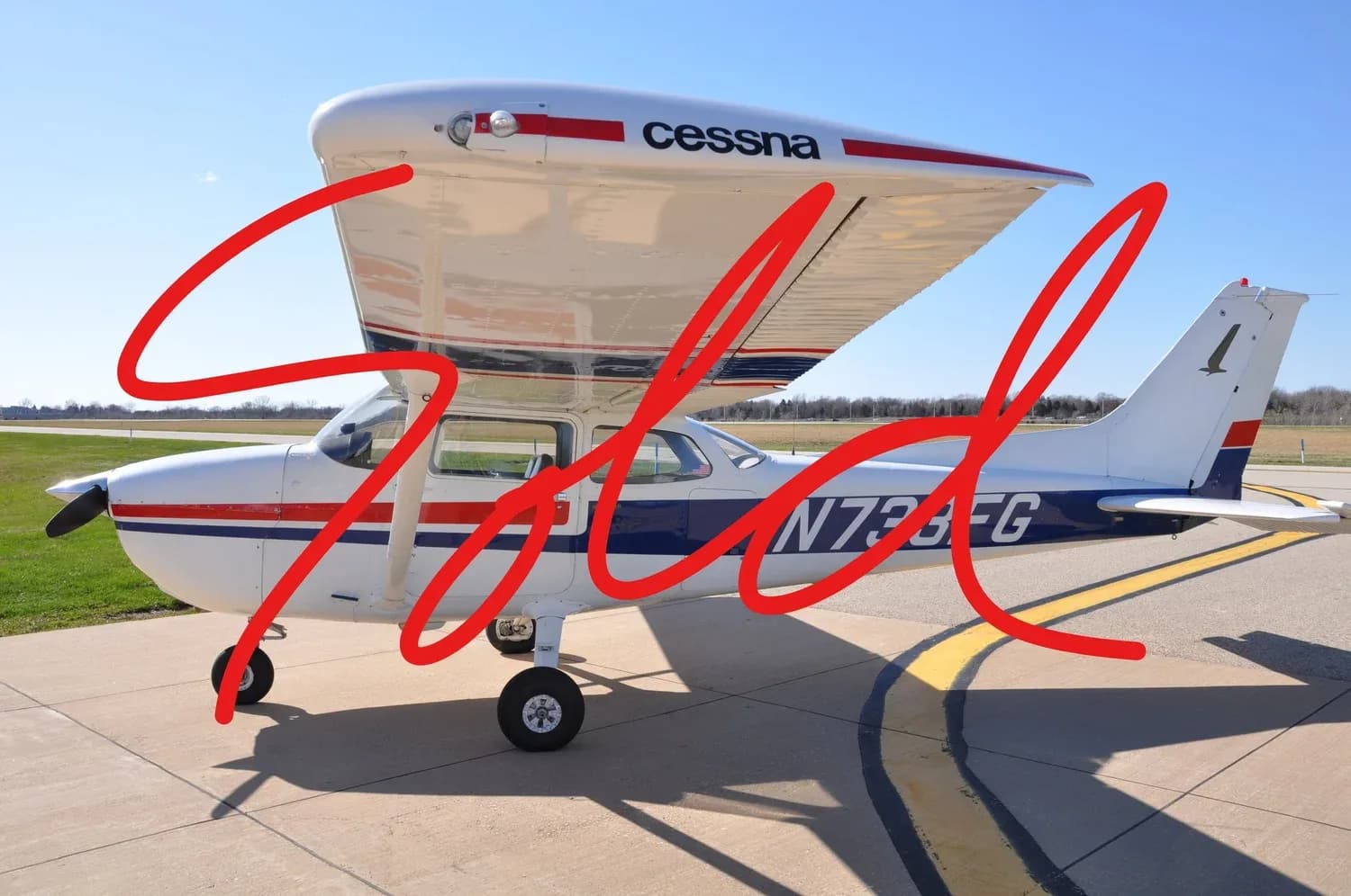 A white and blue Cessna N733FG aircraft with "Sold" overlaid, parked on an airfield under a clear sky.