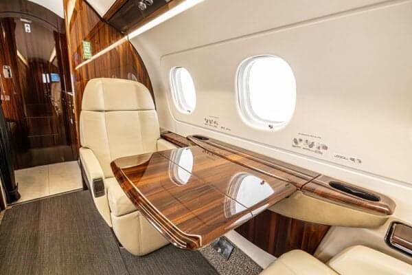 A close-up of a cream-colored seat and a polished wooden fold-out table in the Embraer Legacy 500 cabin.