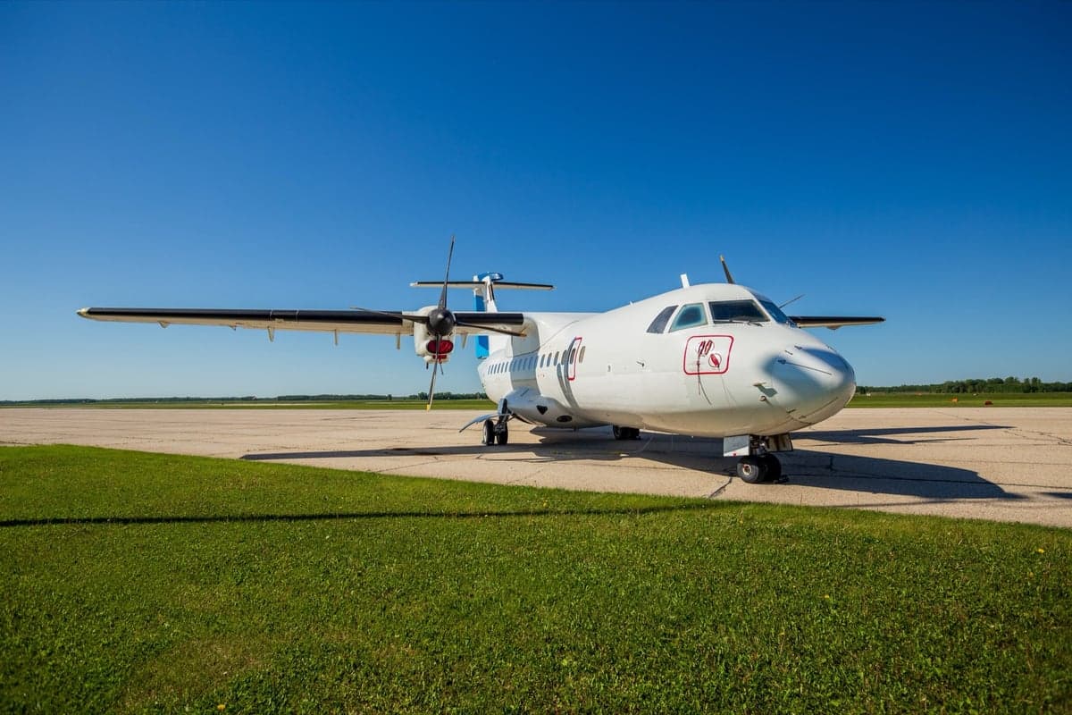 A white turboprop aircraft is parked on the tarmac on a sunny day.