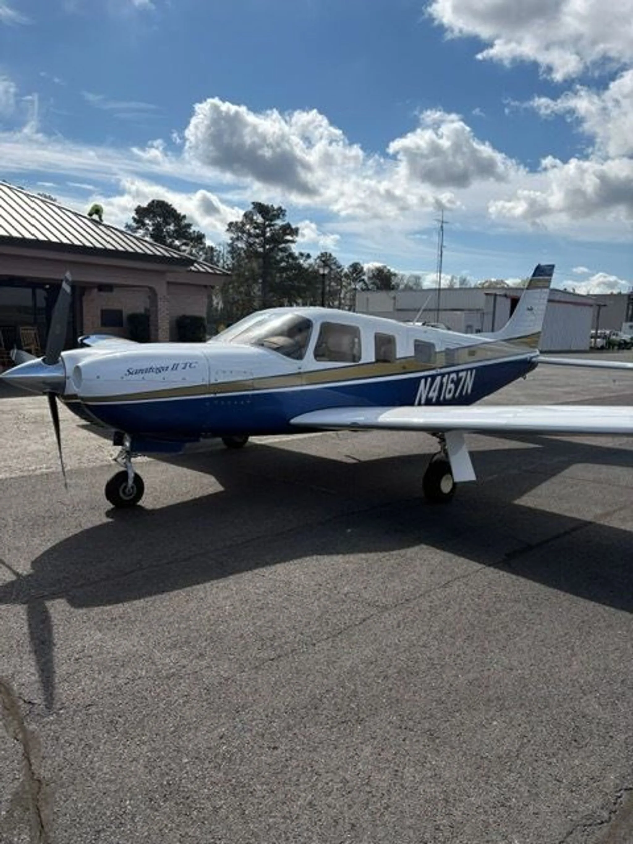 A Piper Saratoga II TC aircraft, N4167N, with white, blue, and gold paint, parked on an asphalt ramp.