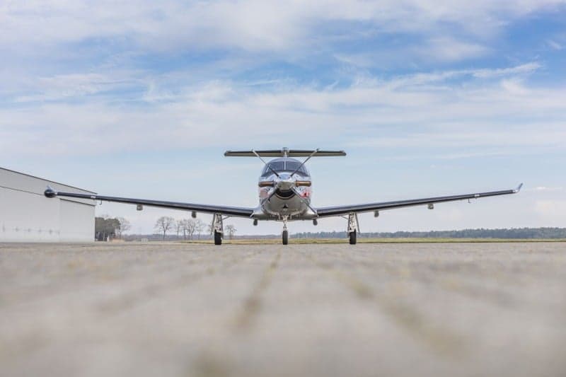 Front view of a Pilatus PC-12 aircraft with a silver and red paint scheme parked on the tarmac.