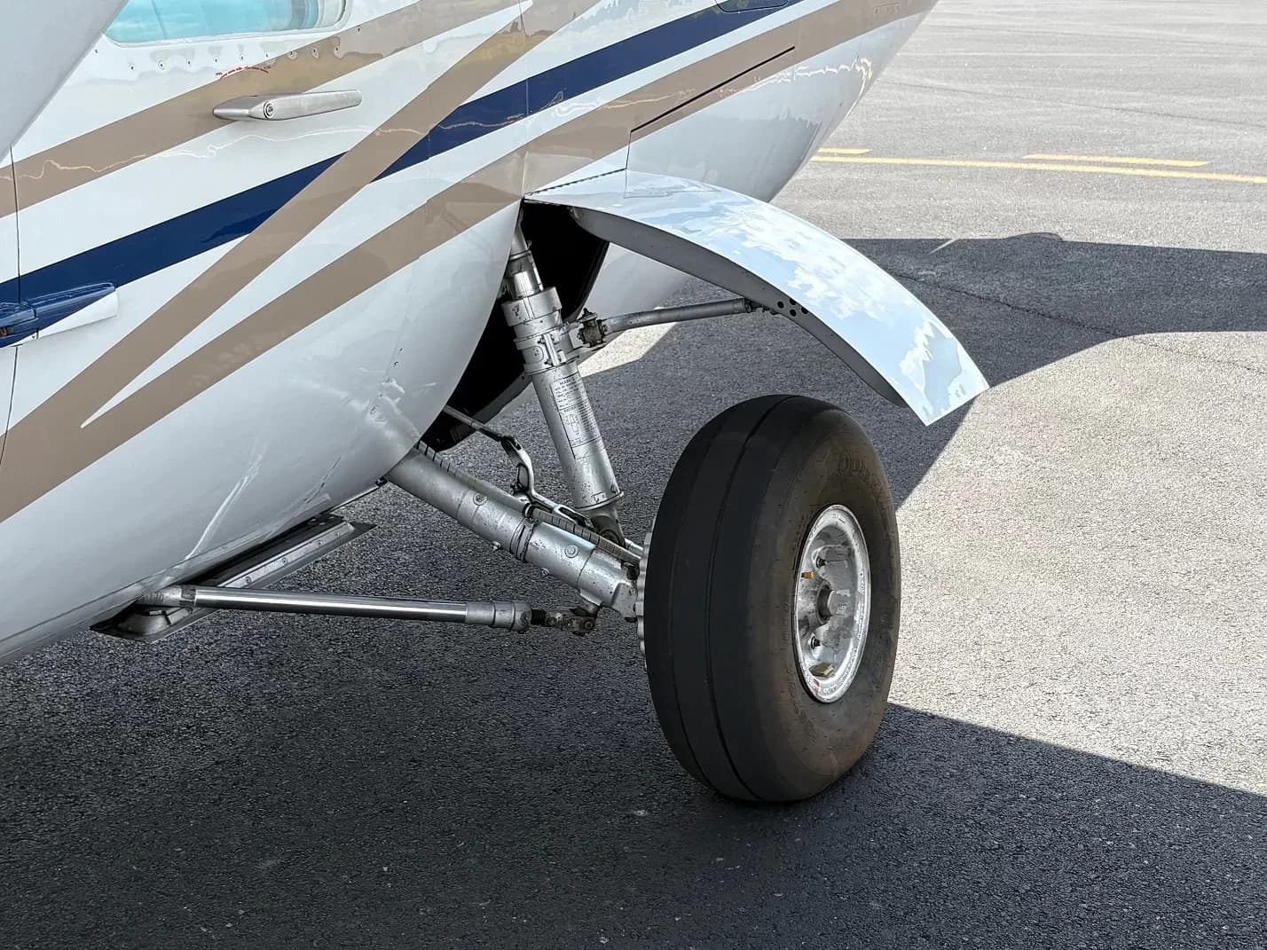 Close-up of the main landing gear and wheel of a white aircraft with blue and gold stripes.