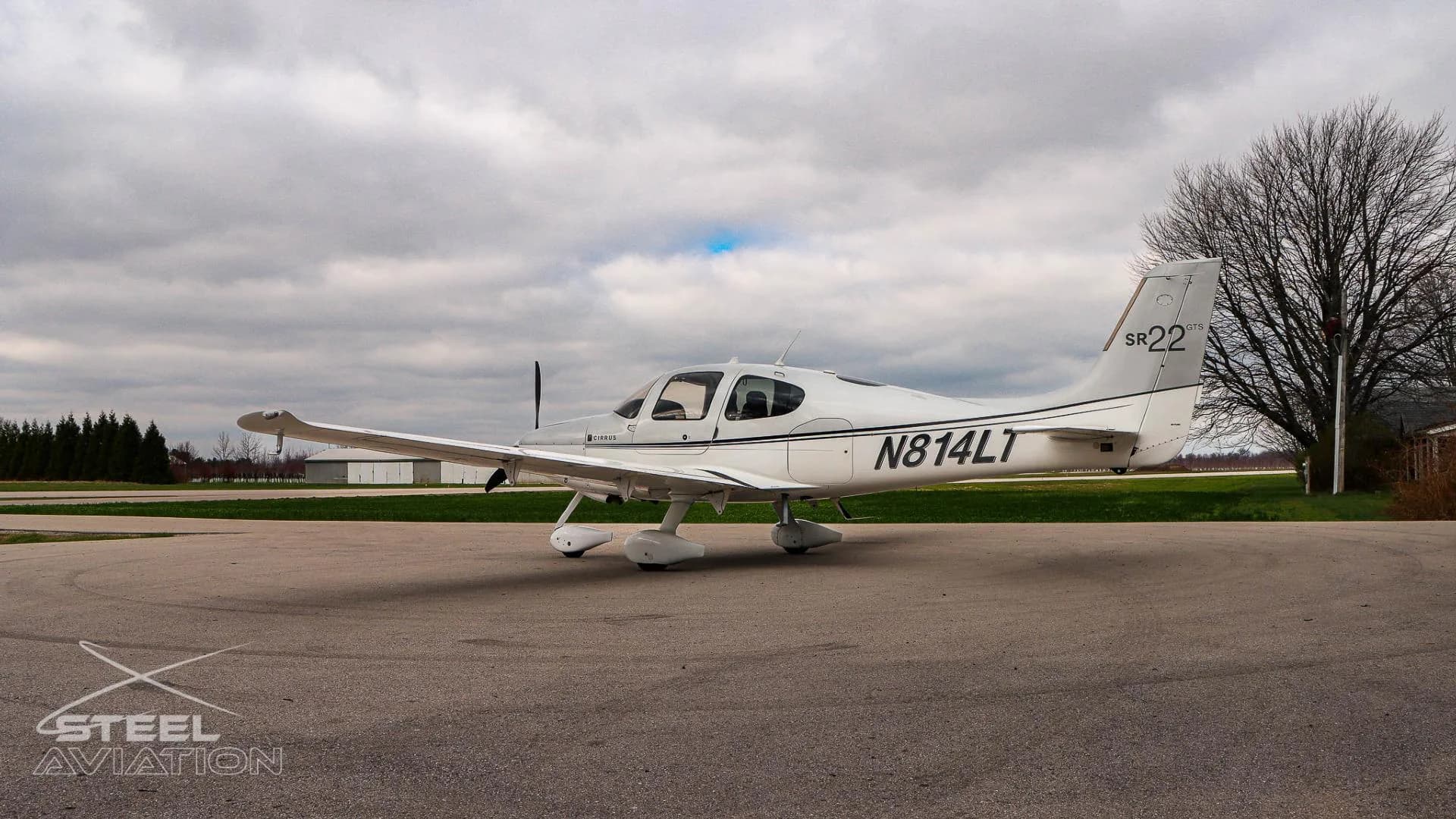 A three-quarter rear view of the white and silver Cirrus SR22 aircraft (N814LT) parked on an apron under a cloudy sky.