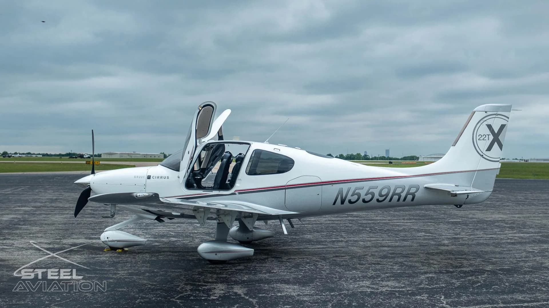 A white and silver Cirrus SR22T aircraft with registration N559RR has its gull-wing doors open on an airfield.