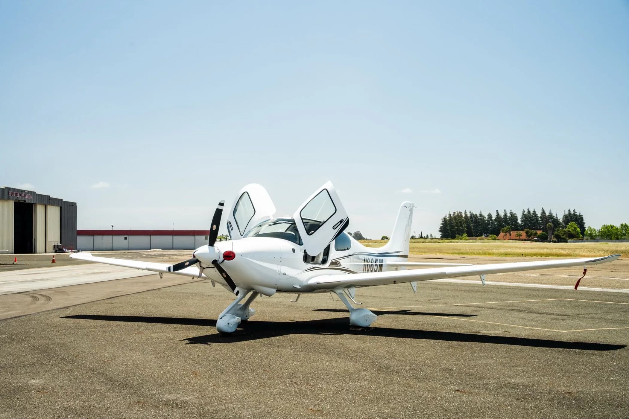 A white Cirrus SR22 aircraft with registration N665M parked on the tarmac with both doors open, viewed from the front.