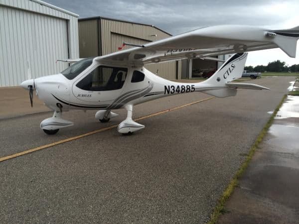 A white CTLS Jubilee aircraft is parked on the tarmac in front of a hangar.