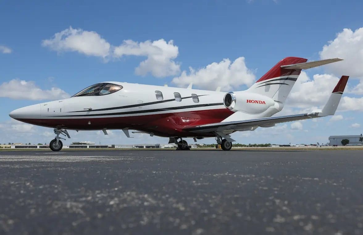 A white and red HondaJet HA-420 business jet with black stripes on a tarmac under a blue sky.