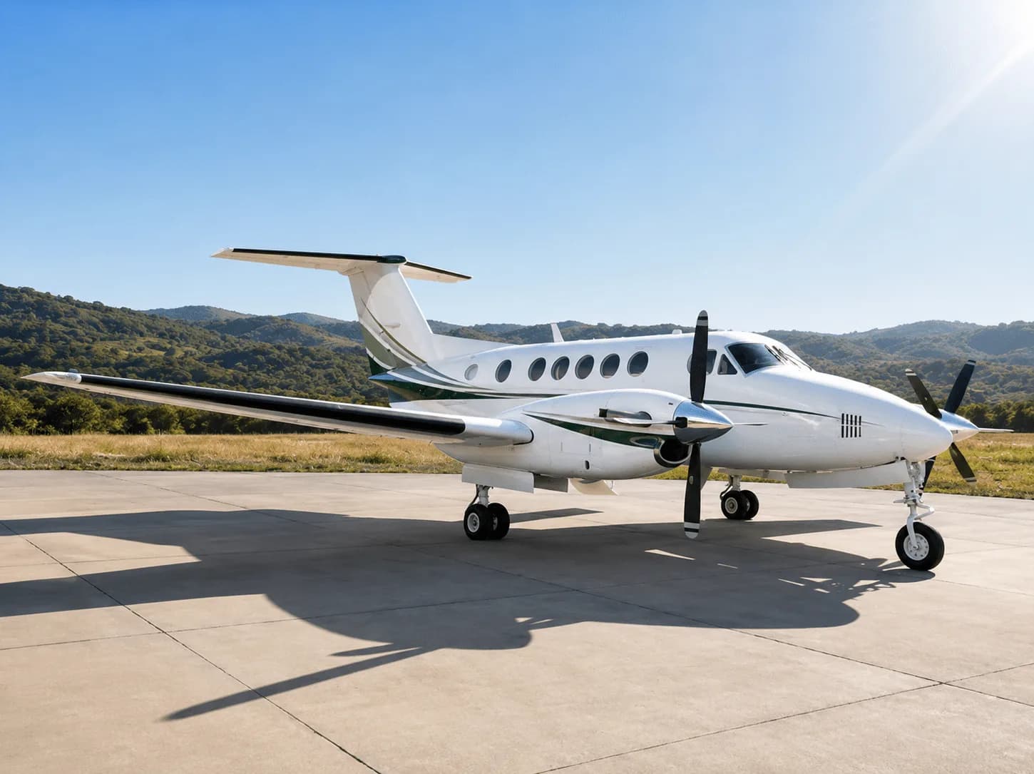 A white twin-turboprop aircraft with green and black stripes is parked on a concrete tarmac under a clear blue sky with hills in the background.