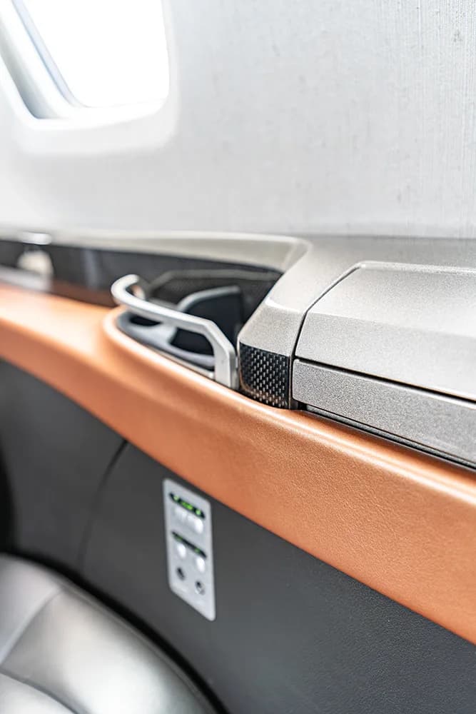 A close-up of the aircraft cabin interior showing a side panel with controls and a cup holder.