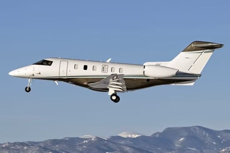 A light jet aircraft in flight over a mountainous landscape.