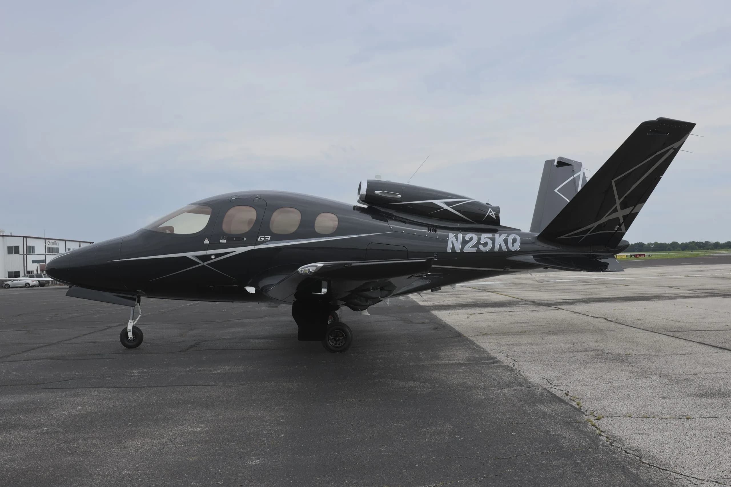 A black Cirrus Vision Jet (N25KQ) with white and grey accents is parked on a tarmac under a cloudy sky.