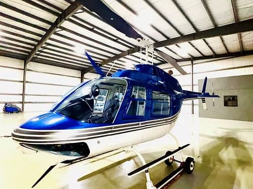 Side view of a blue and white Bell 407 helicopter parked in a hangar.