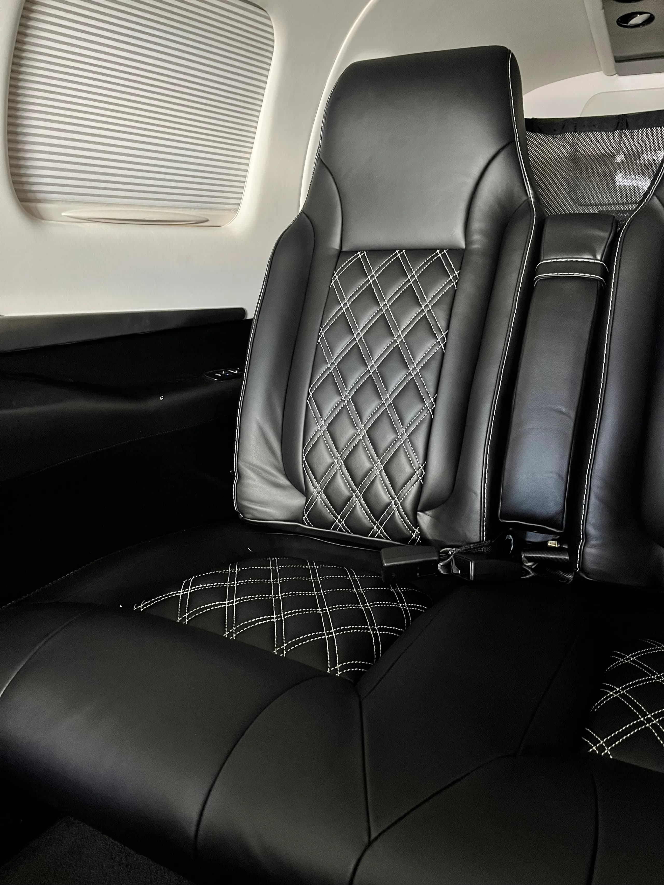 A close-up view of a black leather aircraft cabin seat with white diamond stitching.
