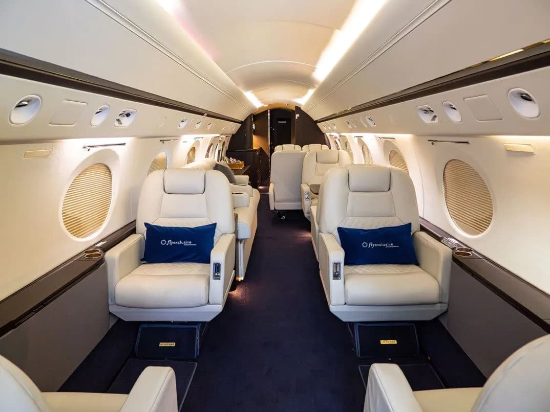 Aircraft interior with white leather seats and blue carpet.