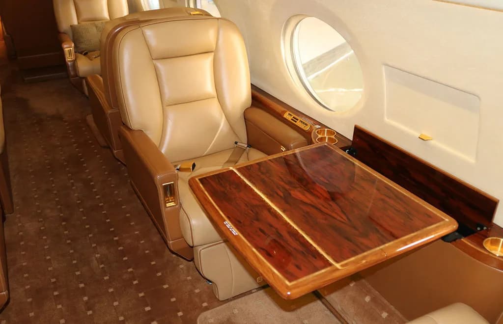 A tan leather seat in a private jet cabin with a polished wood fold-out table extended.