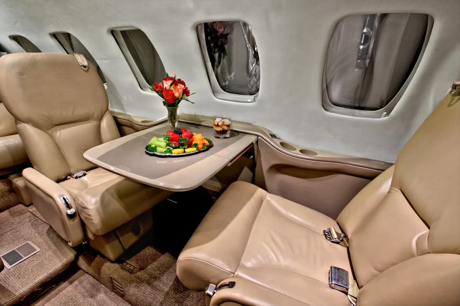 A view of the interior of a jet with tan leather seats and a table with food.