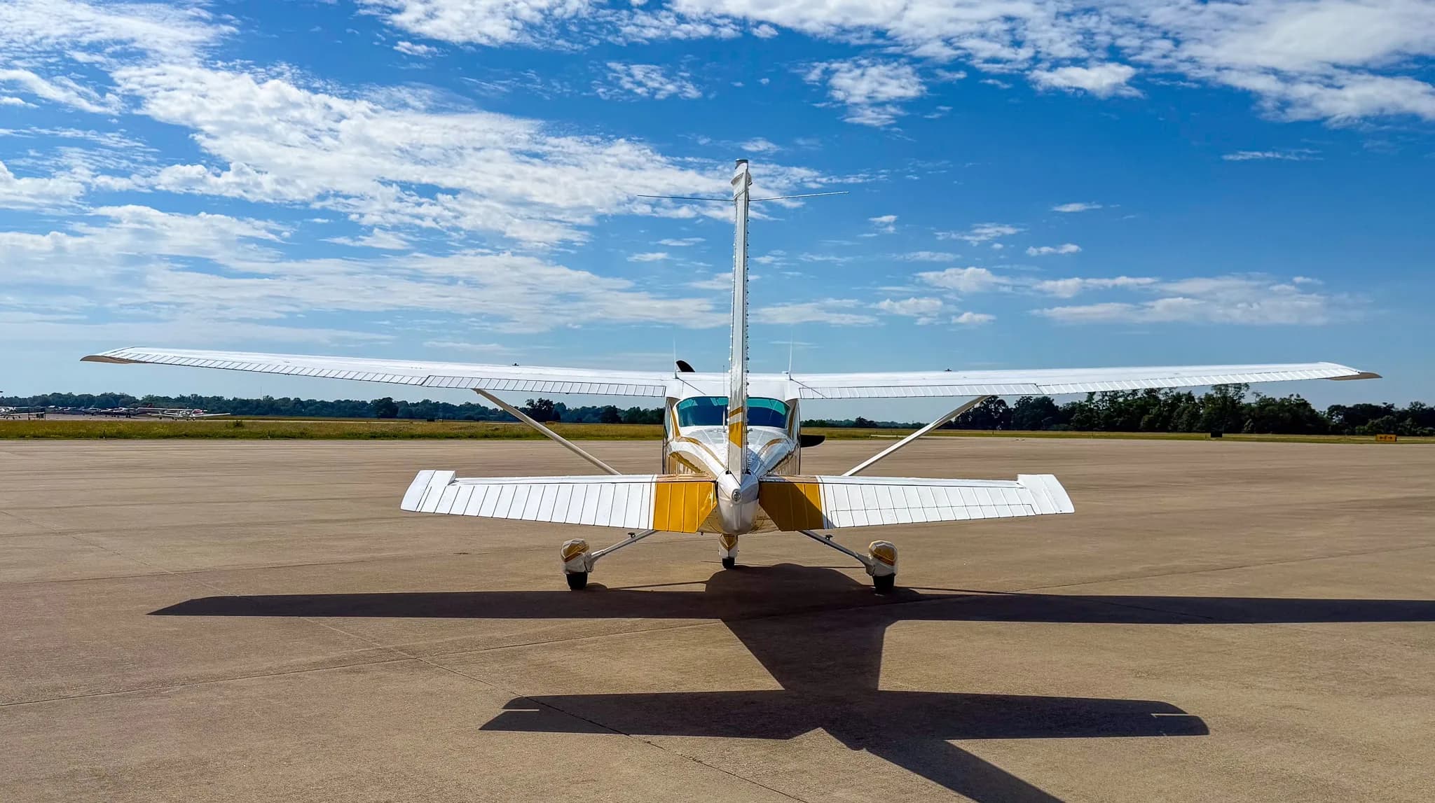 The rear view of a white and gold Cessna Skylane N7489Q parked on an airfield tarmac.