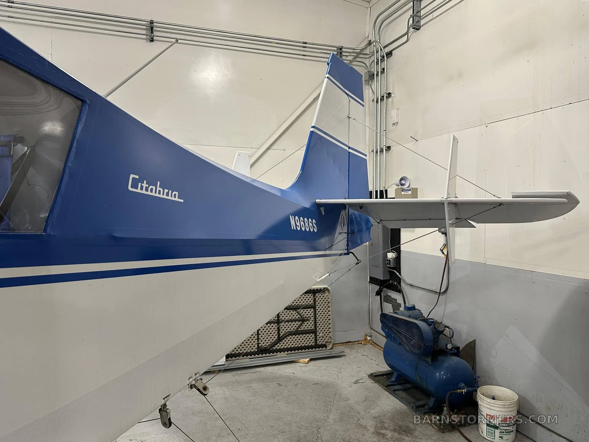 The blue and white tail section of a Citabria floatplane with registration N9686S is shown in a hangar.